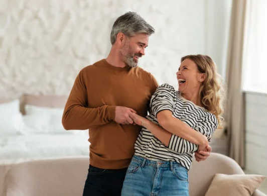 Happy midlife couple laughing together at home, representing healthy relationships and emotional connection in your 40s and 50s.