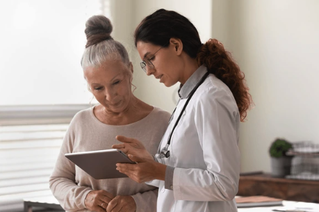 Older woman talking with female doctor holding an ipad advocating for menopause care, hormone health, and patient empowerment.